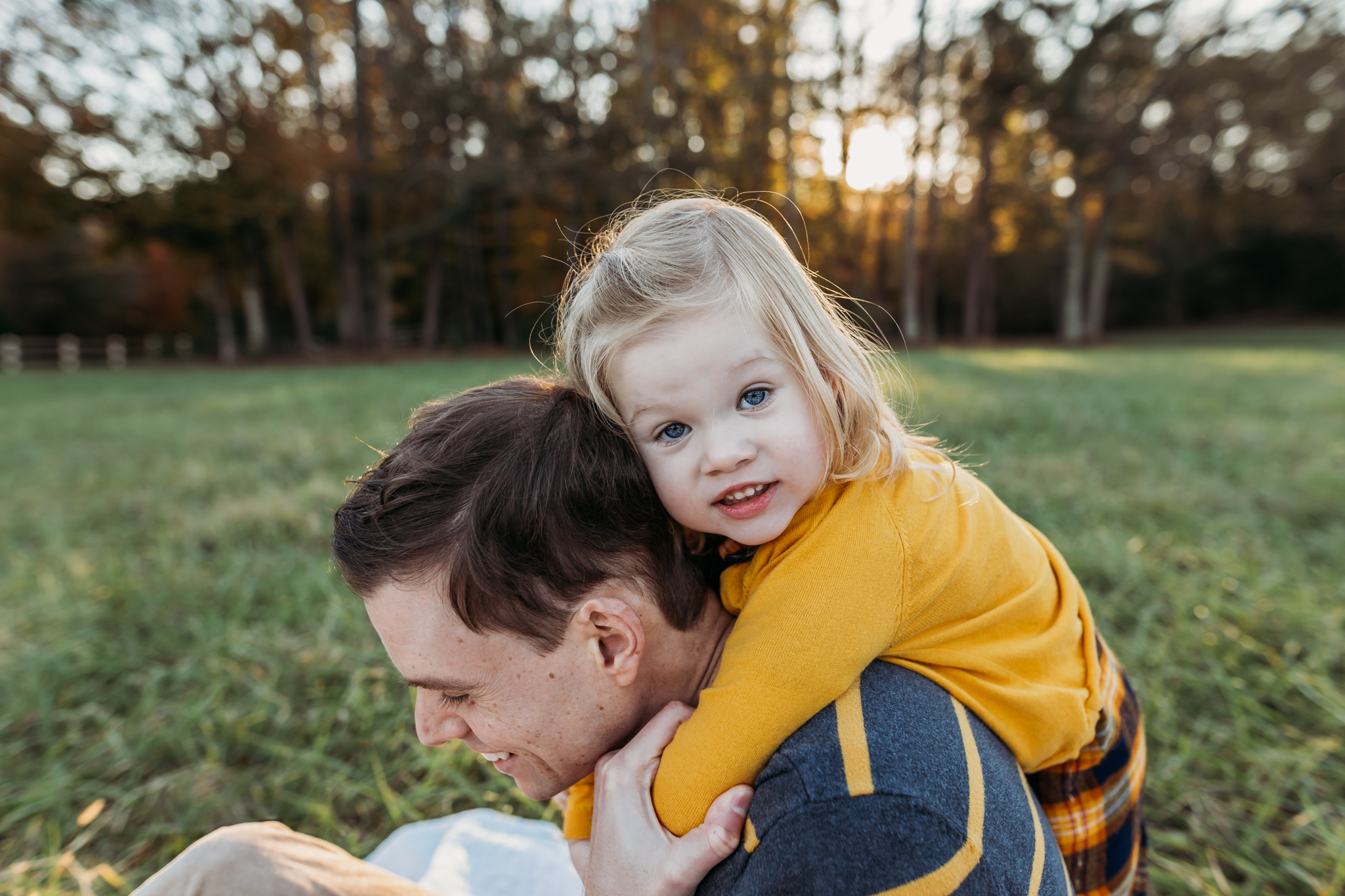 little girl hugs dad from behind in a field