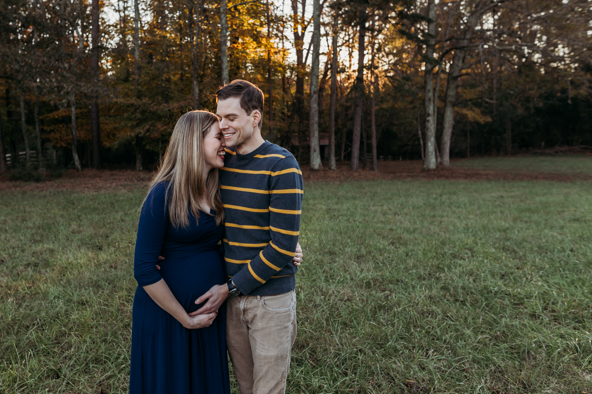 couple laugh while embracing pregnant belly during maternity photos