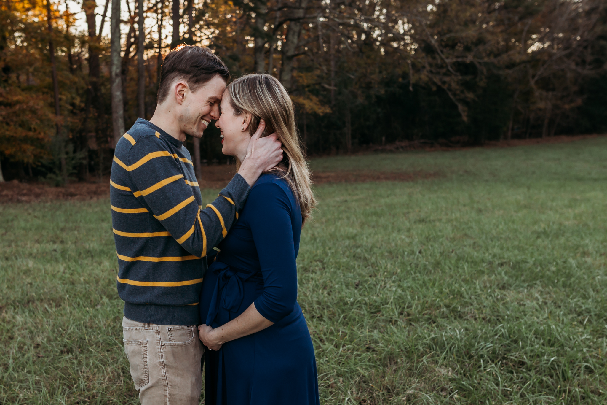 couple embraces while mom hold pregant belly photos