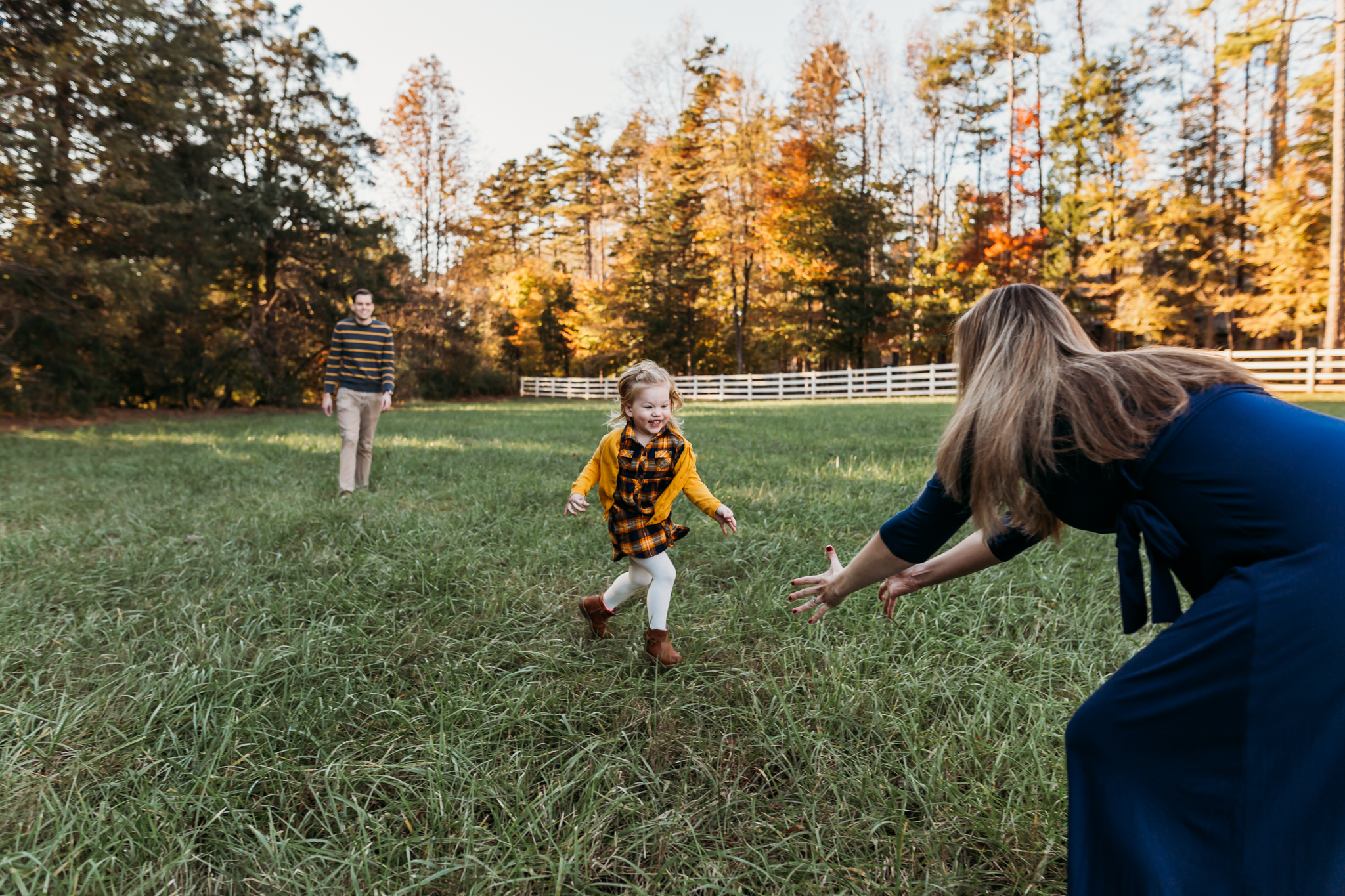 daughter running to mother in a field while dad watches