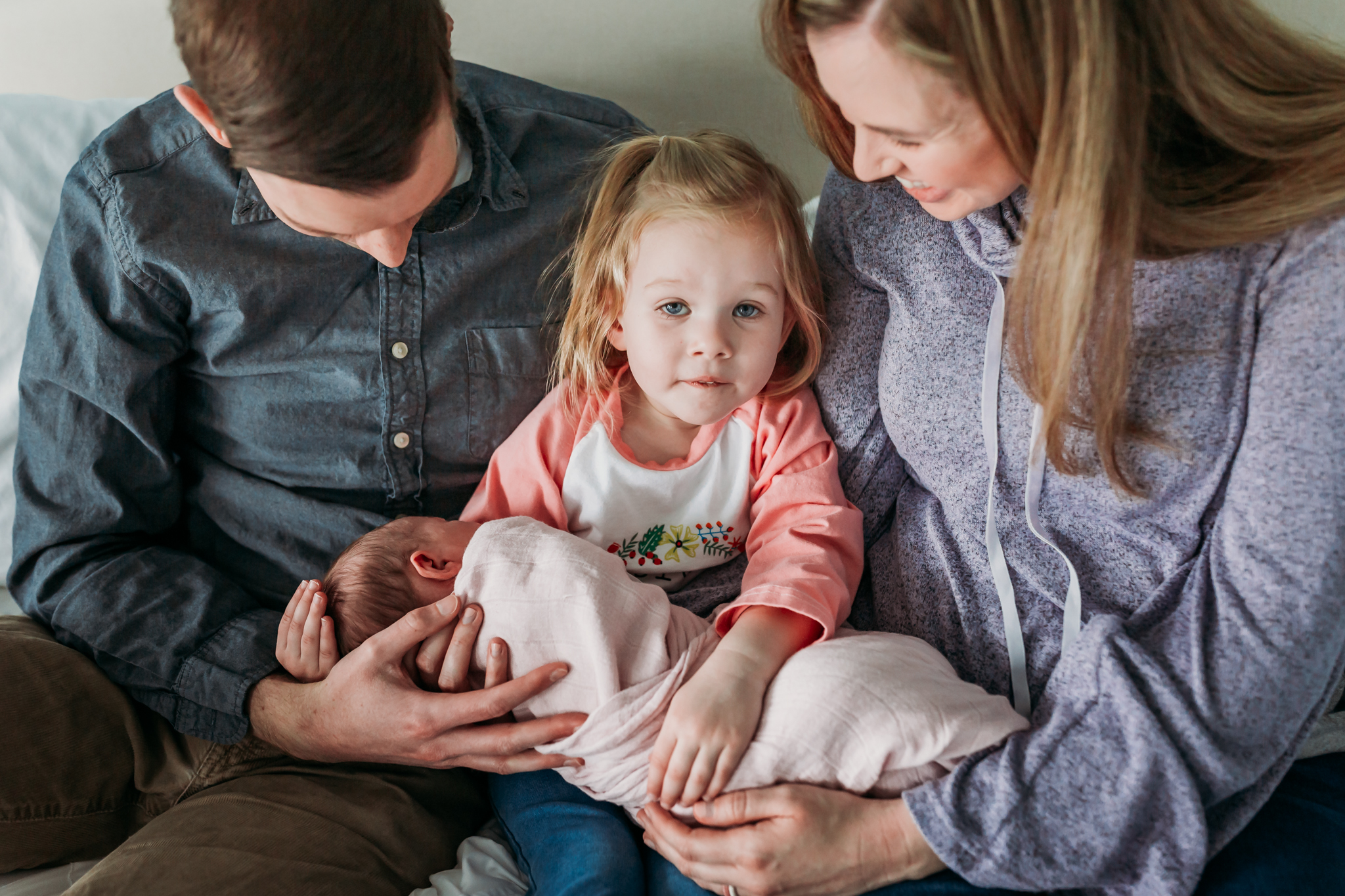 sister holds newborn and looks at camera surrounded by parents