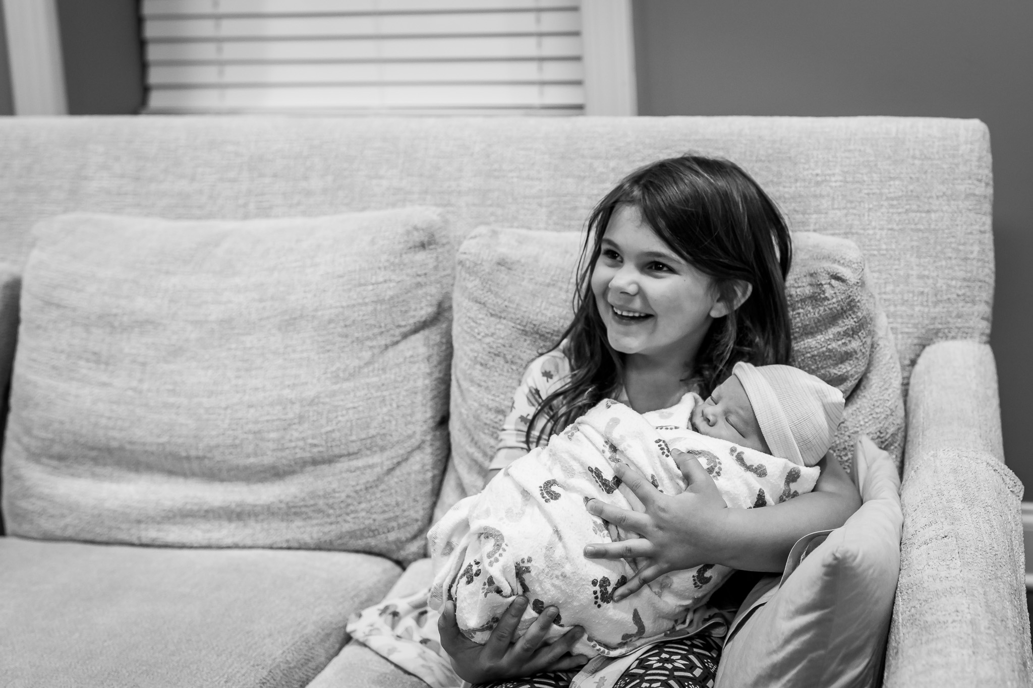 sister smiles as she holds newborn brother
