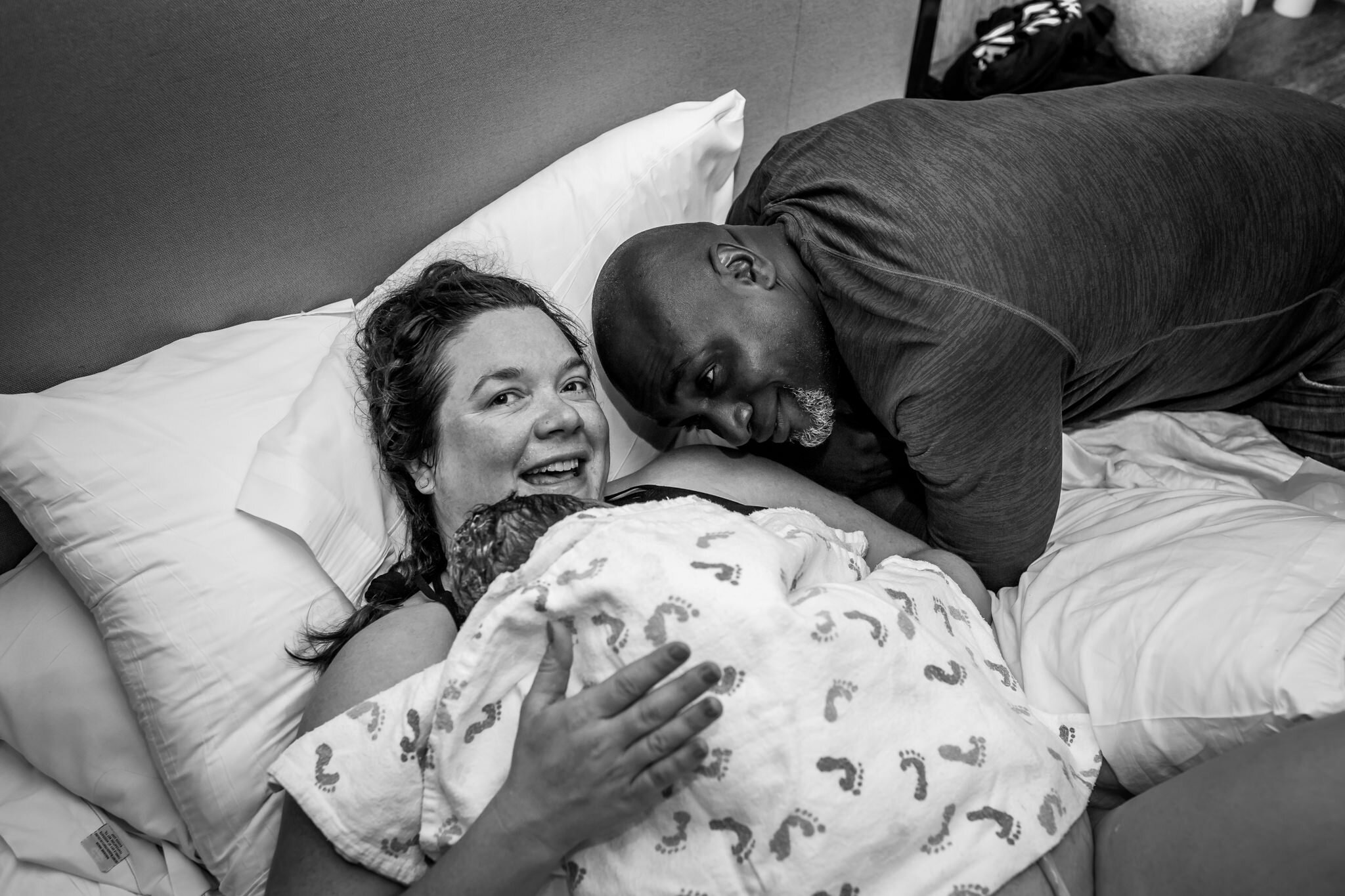 mother smiles as newborn lays on her chest postpartum