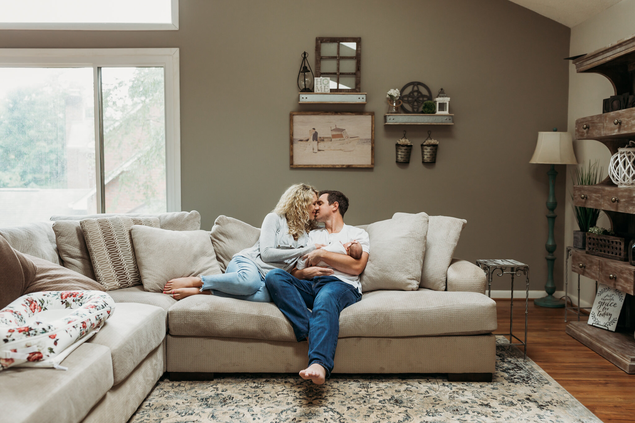 parents kissing on couch with newborn baby