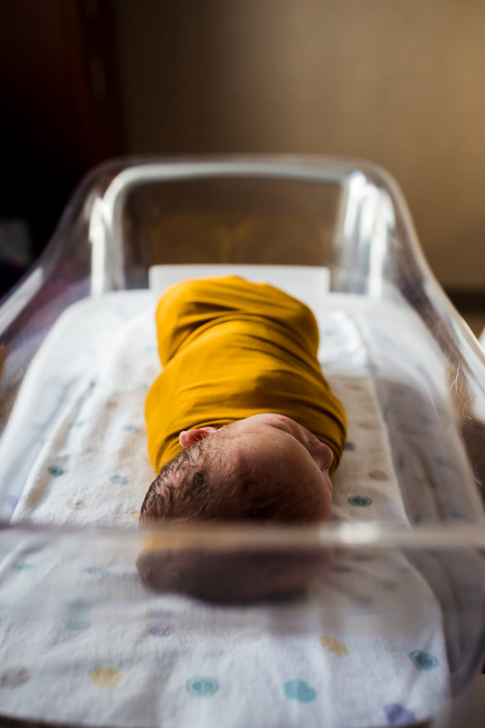 fresh 48 baby in yellow swaddle in hospital bassinet