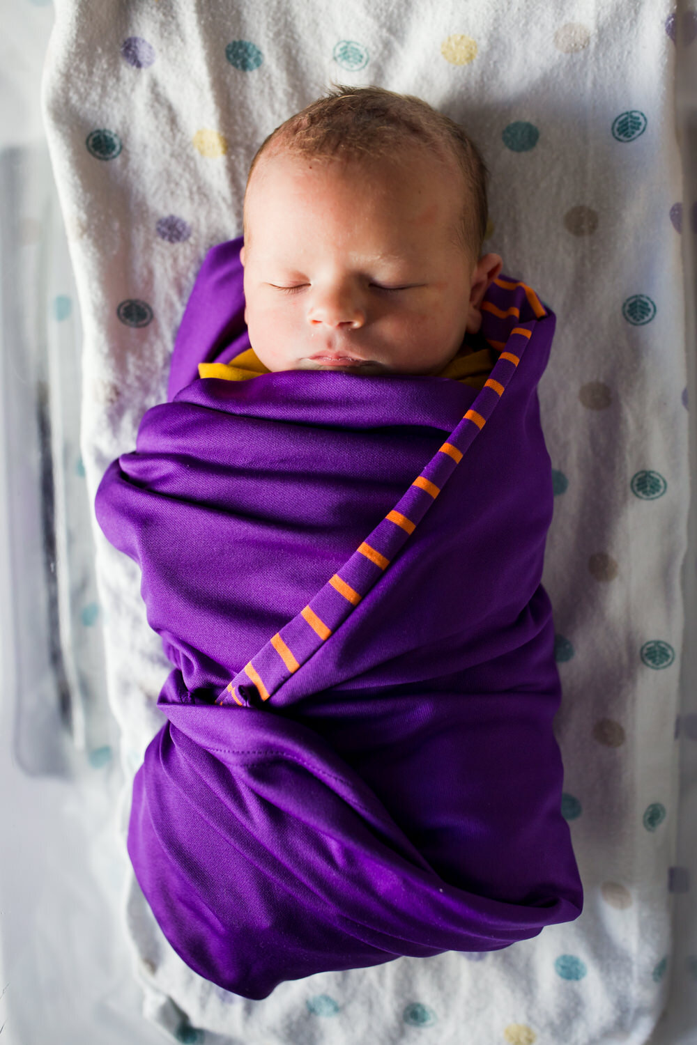 newborn wearing purple shirt as swaddle blanket