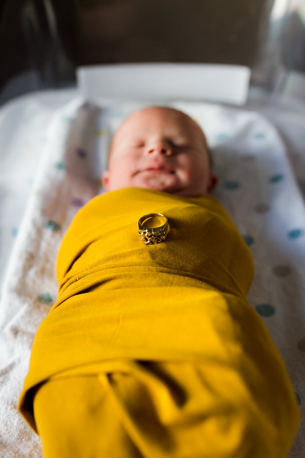 yellow swaddle baby with gold ring in hospital bassinet