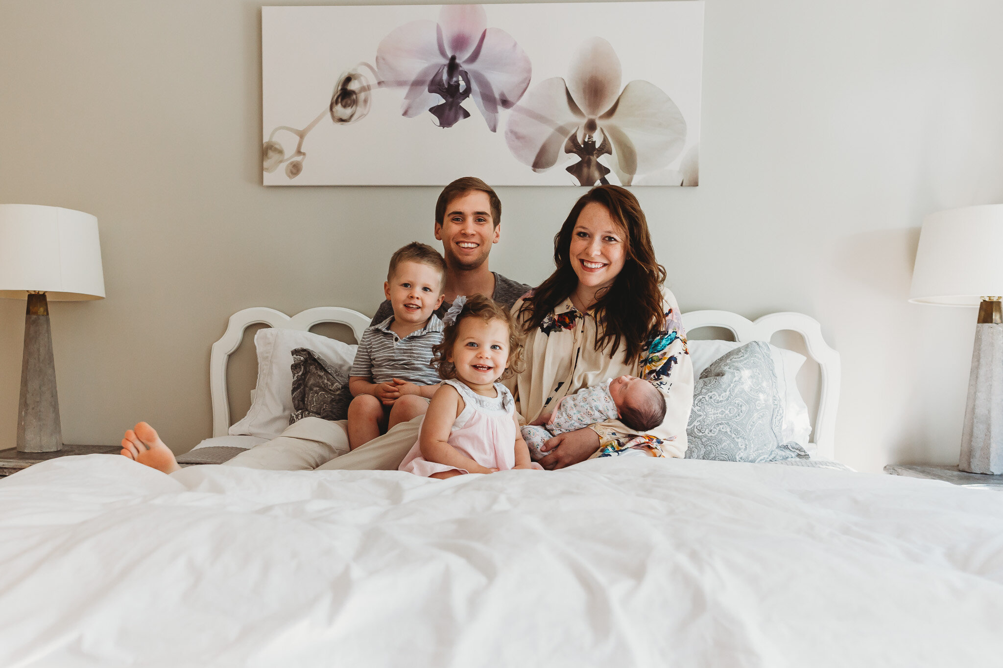 family sitting on bed surrounding baby lifestyle newborn