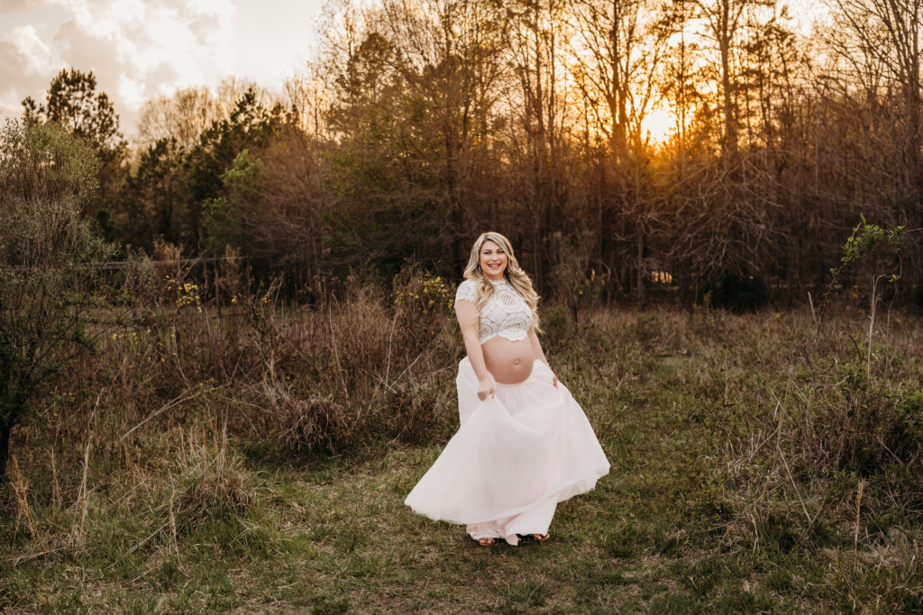 Pregnant mom in pink tulle skirt in field at sunset