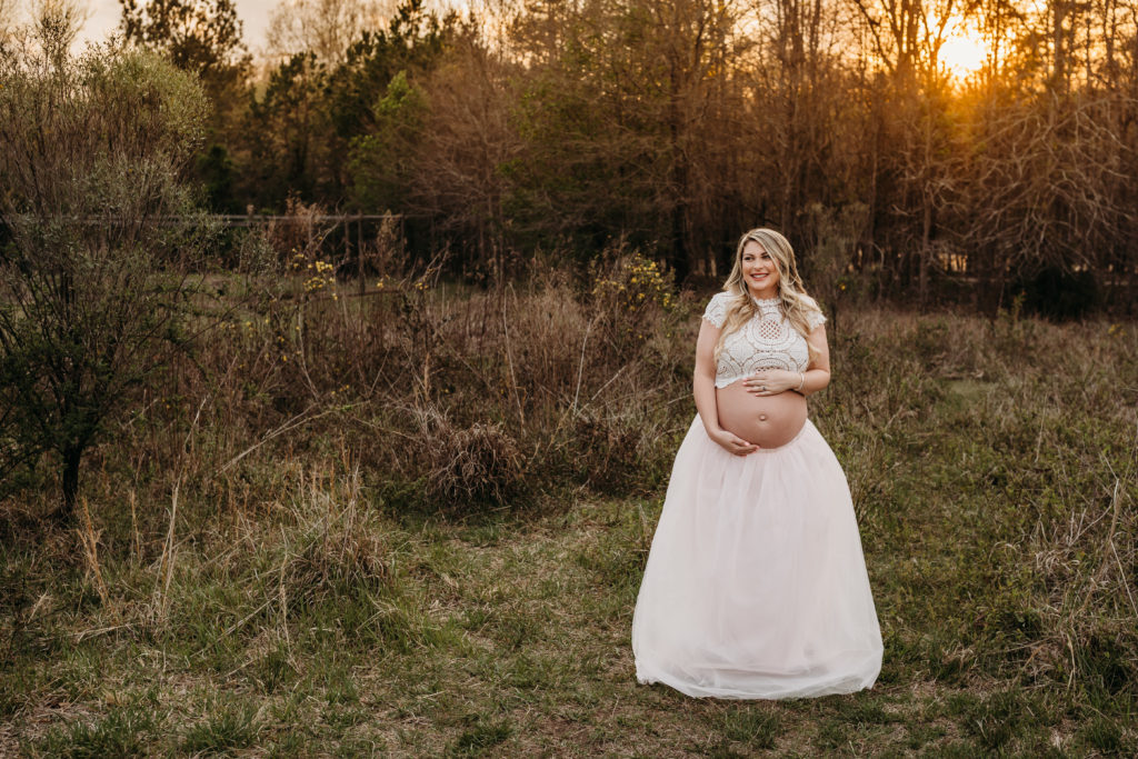 Pregnant mom in pink tulle skirt in field at sunset
