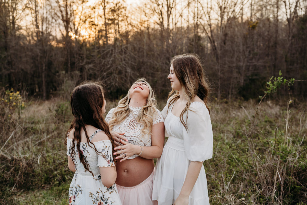 Pregnant mom in pink tulle skirt laughing with her daughters