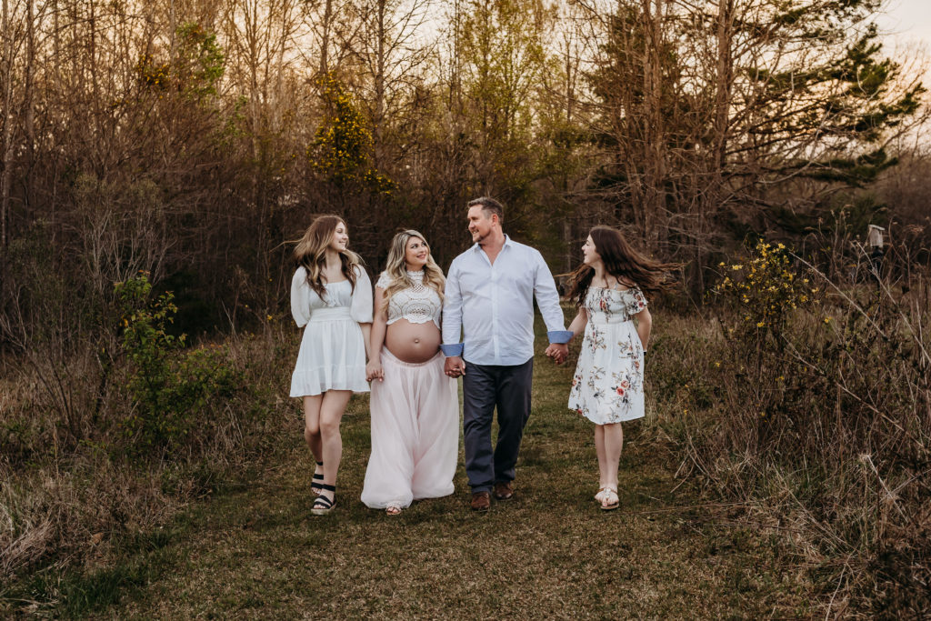Family of 4 walking in field during maternity session