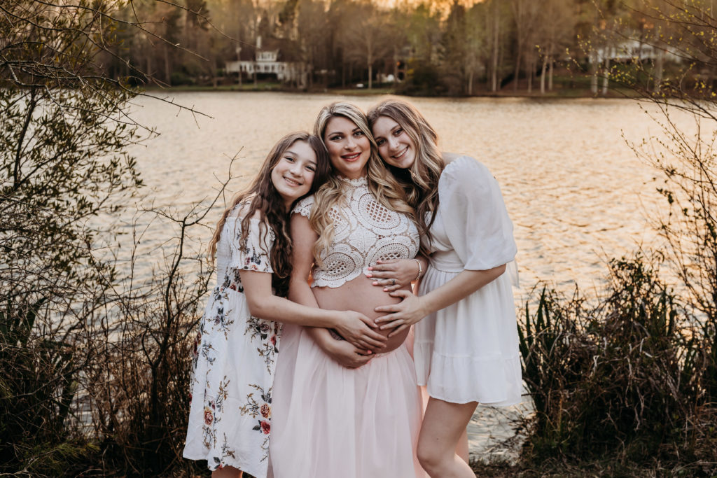 Pregnant mom hugging her daughters near water