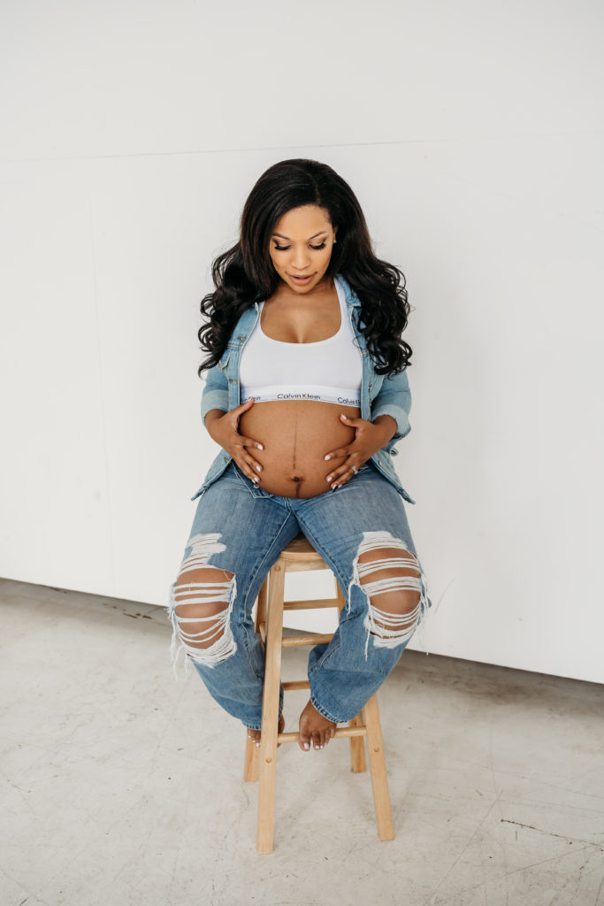 Woman dressed in denim looking down and cradling her pregnant belly