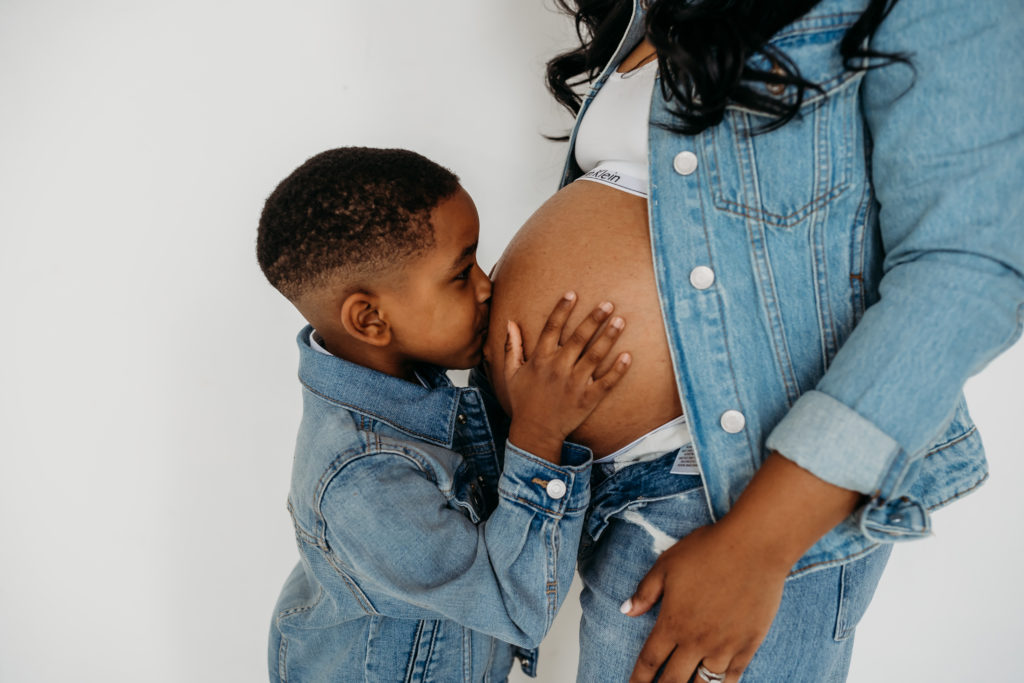 Son kissing moms exposed pregnant belly both dressed in denim