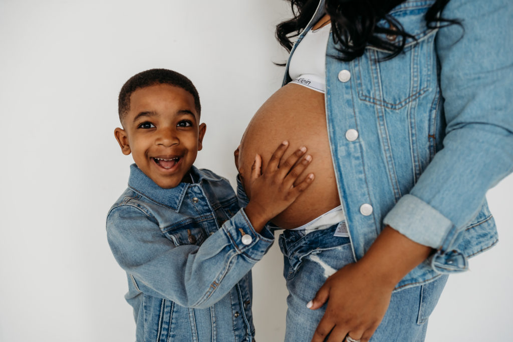 Son holding moms exposed pregnant belly both dressed in denim