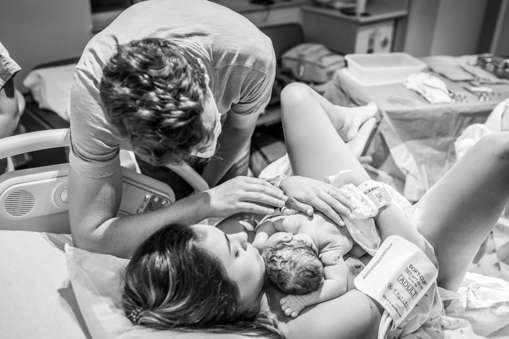 new parents looking at just born baby during hospital birth