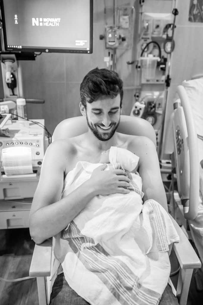 Dad grinning while doing skin to skin with new baby