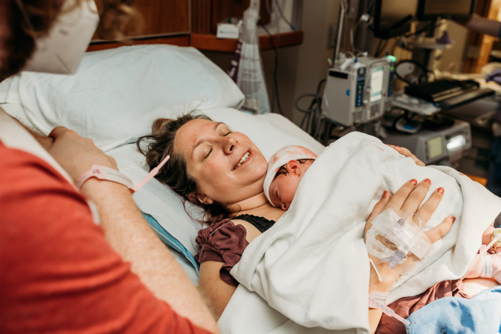 relieved mom holding baby in hospital bed after birth