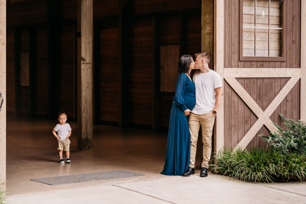 couple kissing in barn while toddler looks on