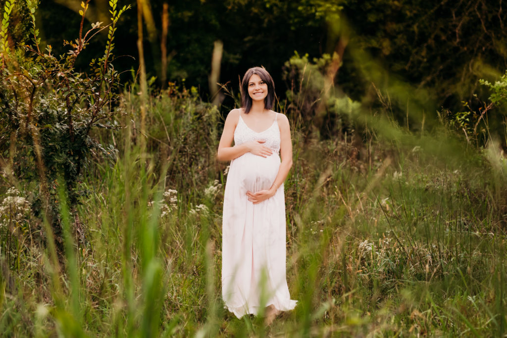 pregnant woman holding her belly in green field