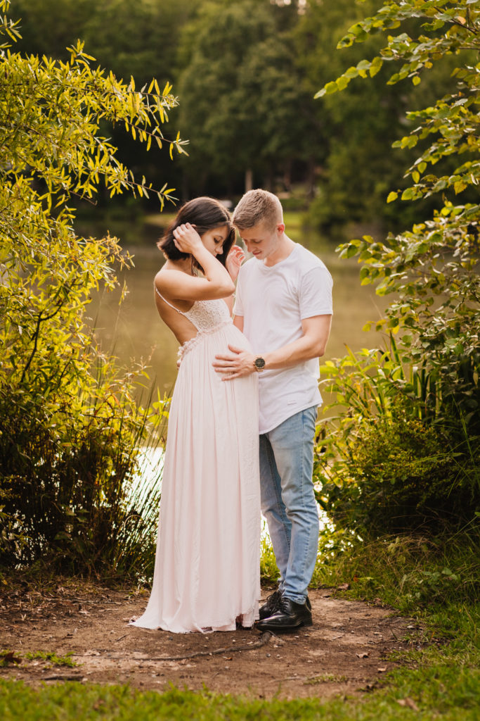 husband cradling wife's pregnant belly near pond