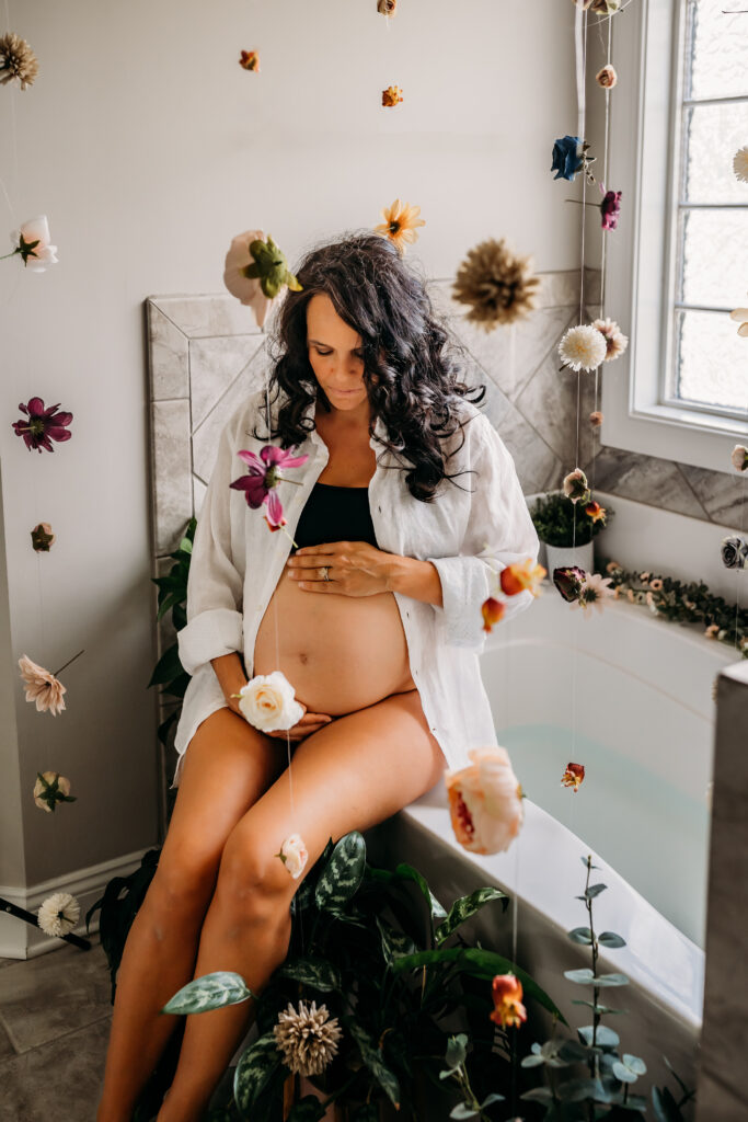 floral maternity milk bath with bare belly with pregnant woman sitting on tub