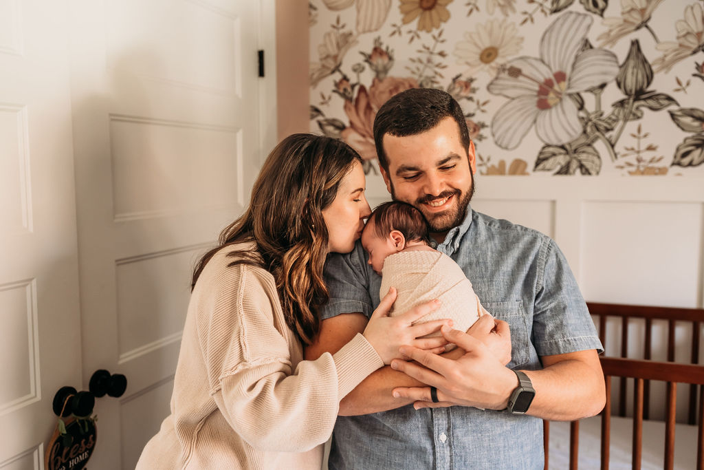 parents kissing baby in nursery during lifestyle newborn session