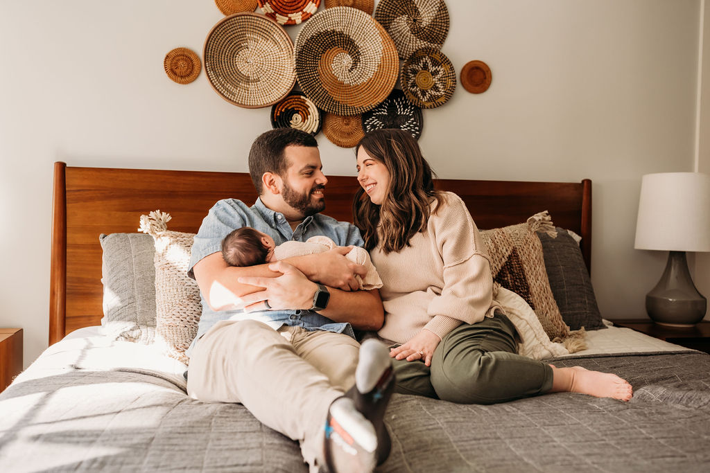 parents snuggling while holding baby in bed during lifestyle newborn session