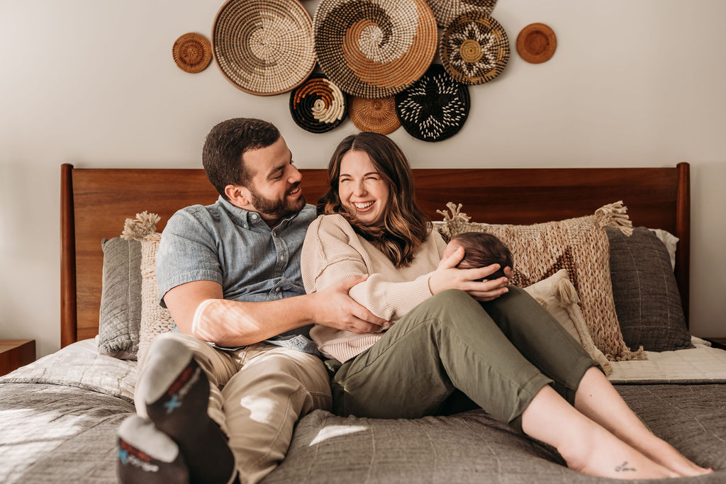 parents laughing while holding baby in bed during lifestyle newborn session