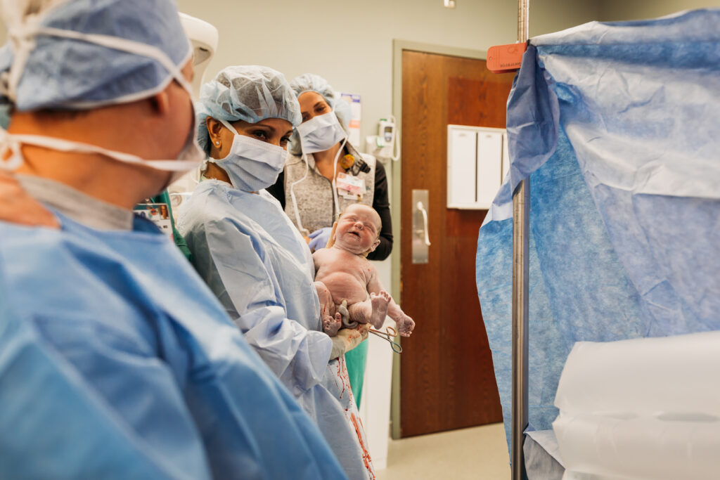 nurse holding up baby during c-section birth
