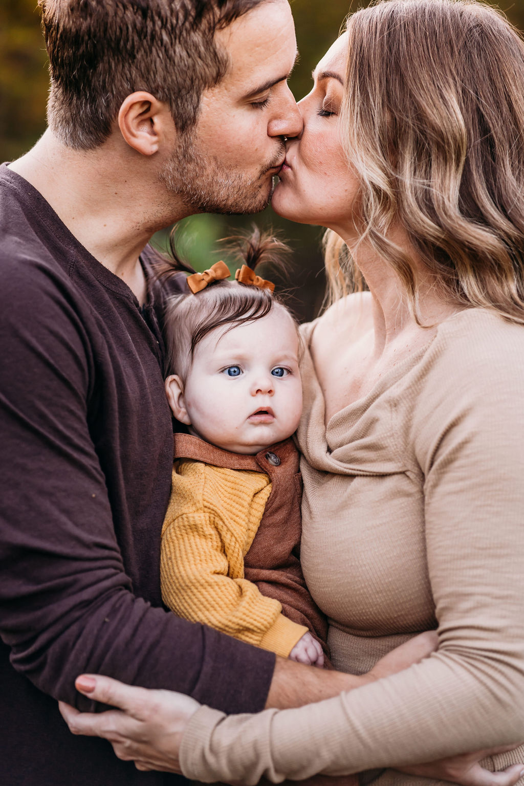 mom and dad kissing while baby is in between them
