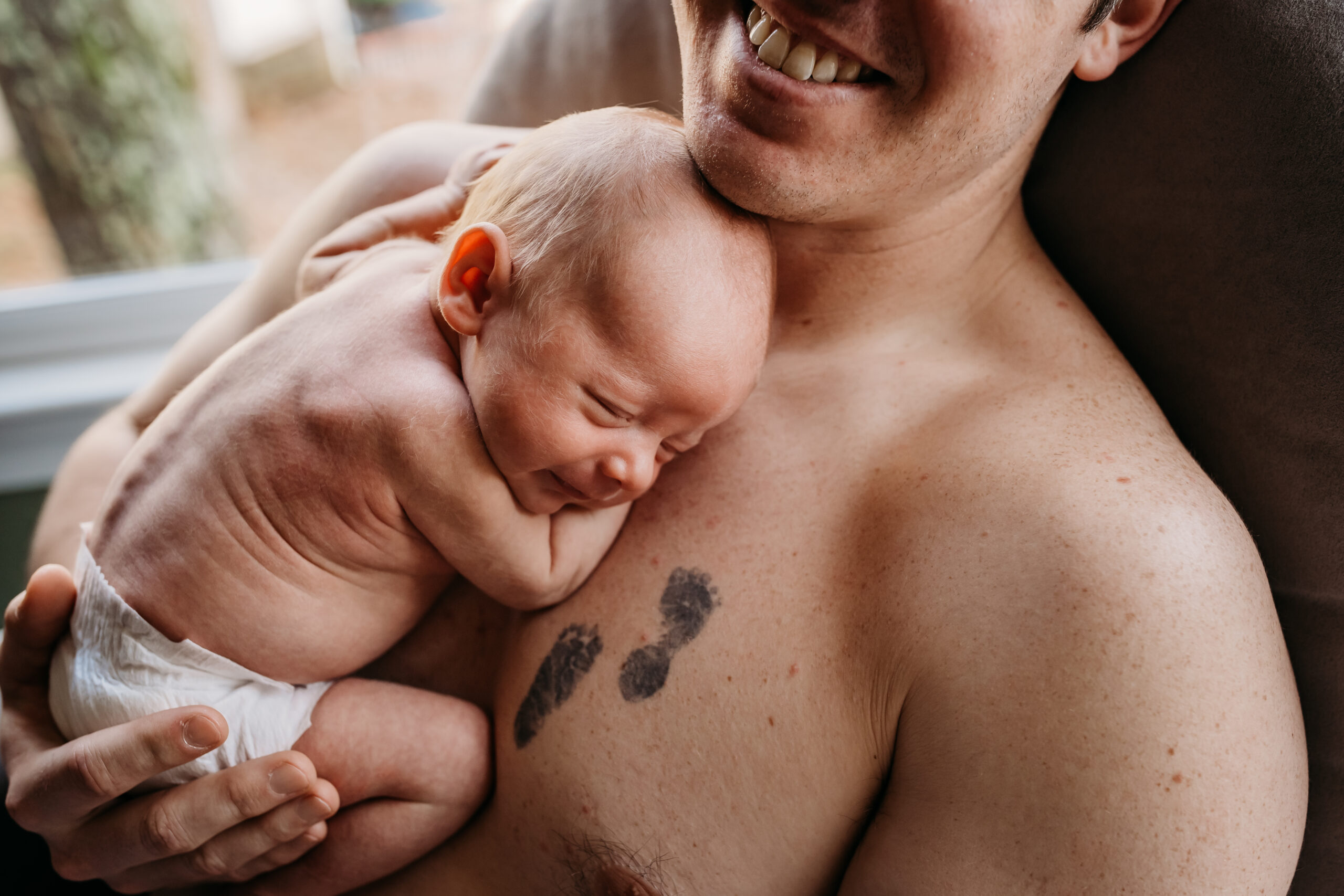 shirtless dad with tattoo holding mostly nude baby