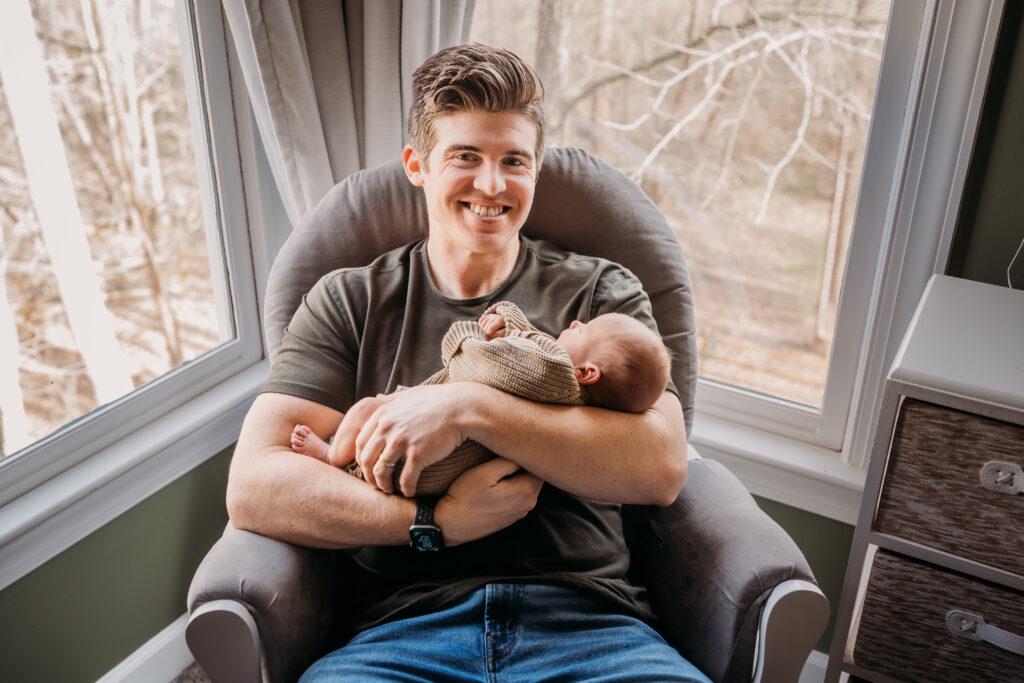 Dad smiling as he holds baby in rocking share bought from baby registry