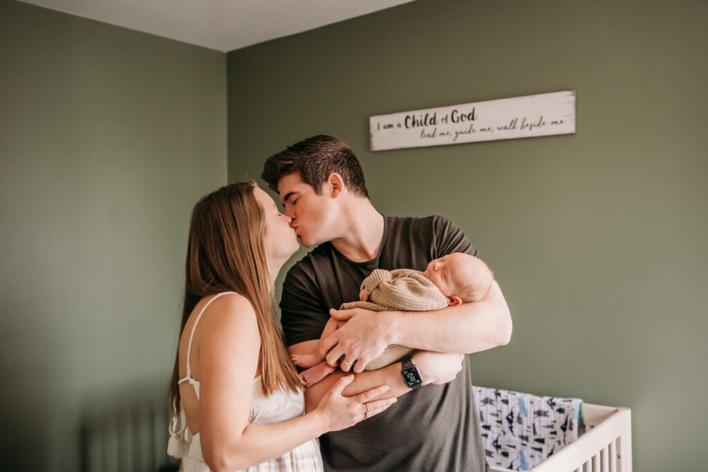 parents kissing while holding baby near crib