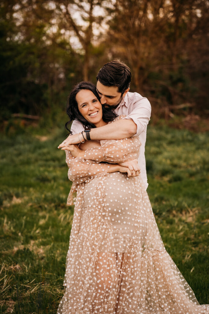 couple embracing in field in favorite maternity dress