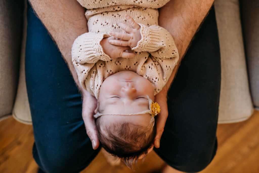 overhead shot of dad holding baby wearing outfit from favorite newborn store