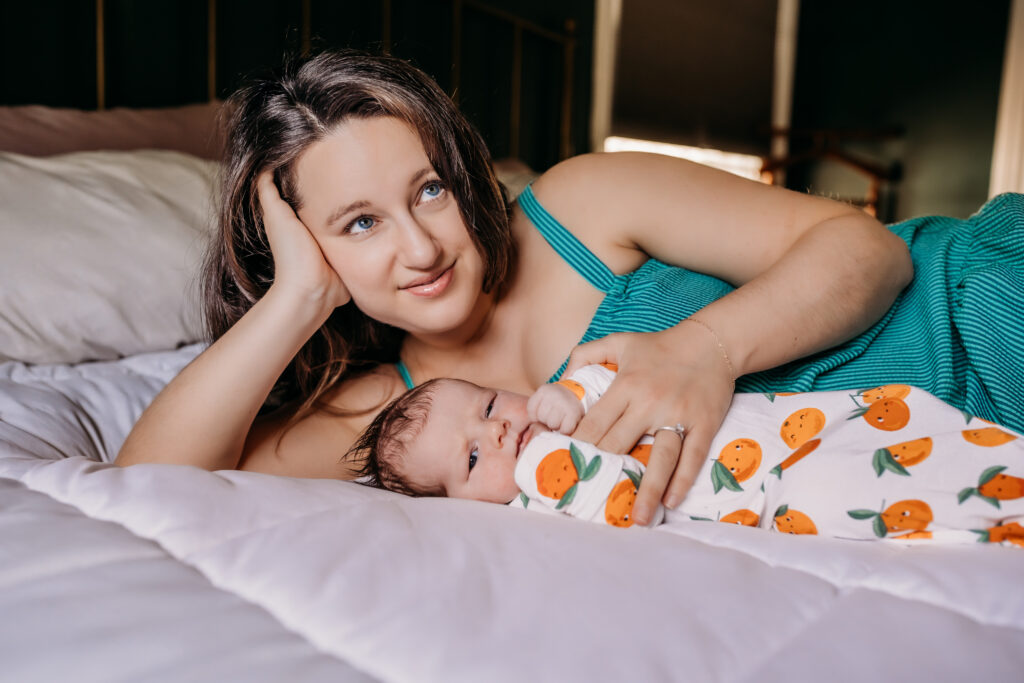 mom laying in bed with baby in an orange onesie