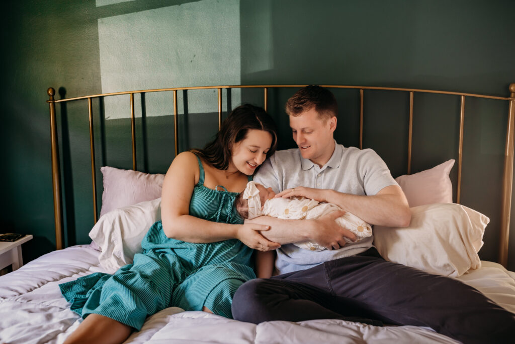 mom and dad snuggling in bed with newborn