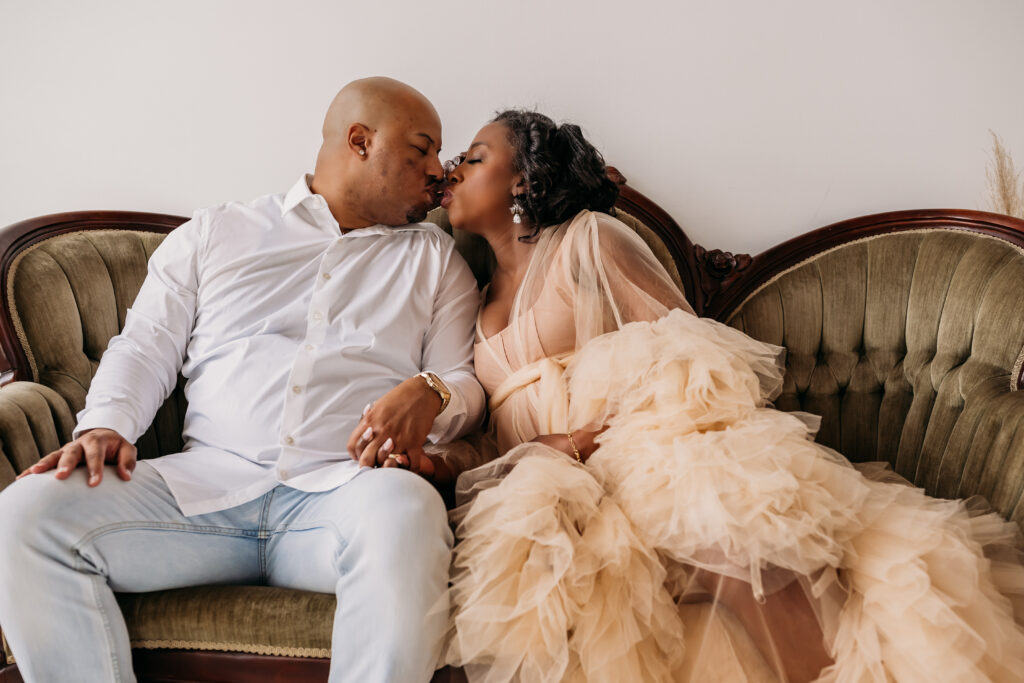 couple sitting on antique couch in cream tulle dress for maternity pregnancy cravings photoshoot