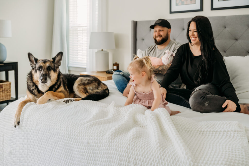 family of 4 sitting on bed with their dog