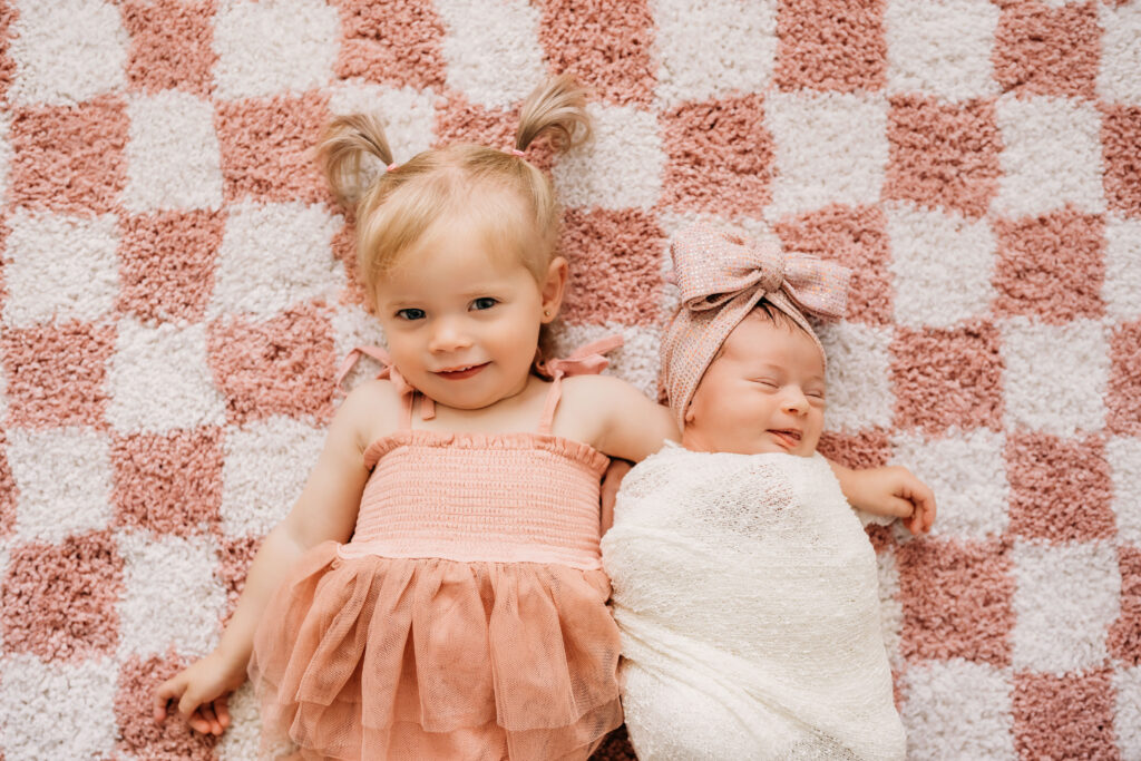 little girl holding newborn sister on checkered rug