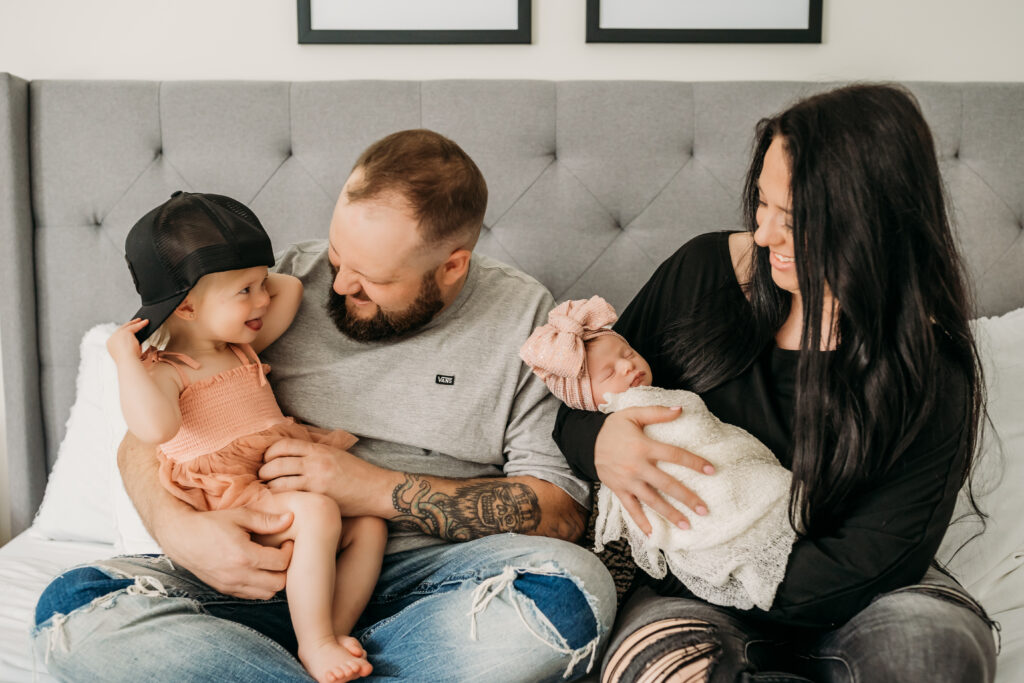 family of 4 sits on bed during newborn photoshoot